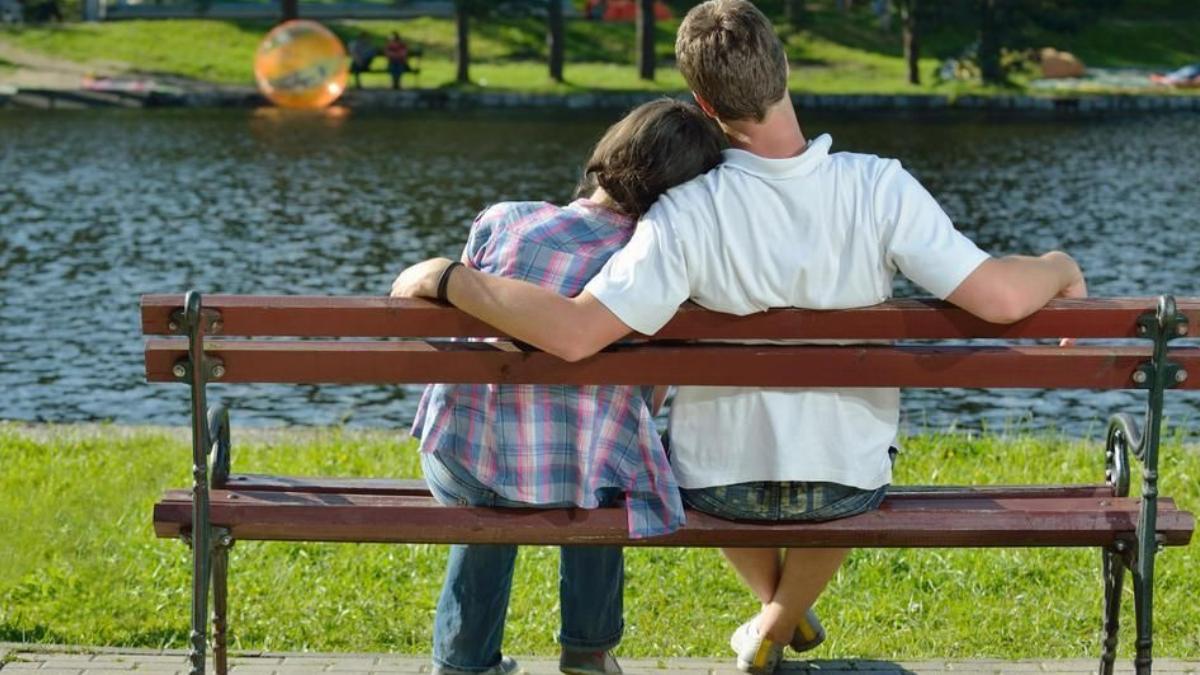 Una pareja de adolescentes, en el banco de un parque.