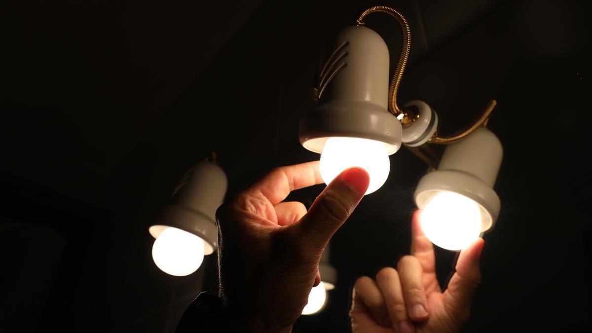 Archivo - Una persona cambia la bombilla de una lámpara
