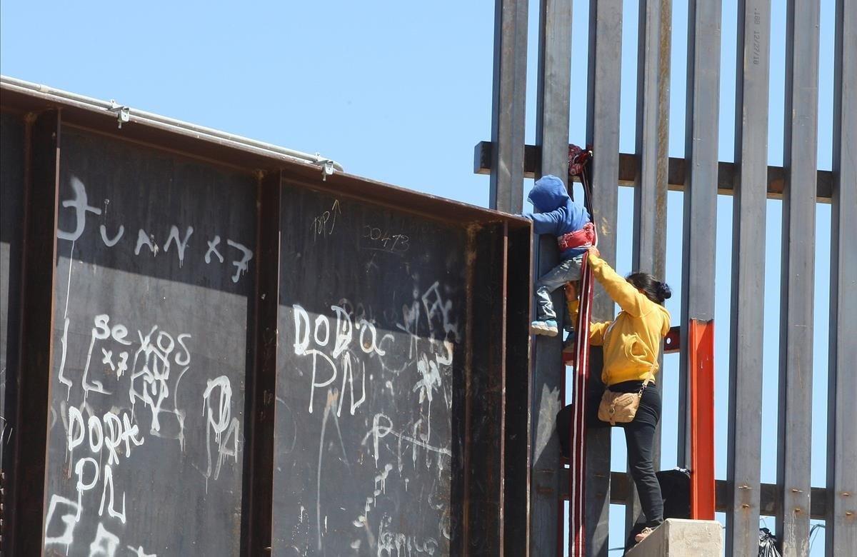 Una mujer ayuda a su hijo a trepar la valla fronteriza que divide a México y Estados Unidos, en el tramo de Puente Negro, en Ciudad Juárez (México).