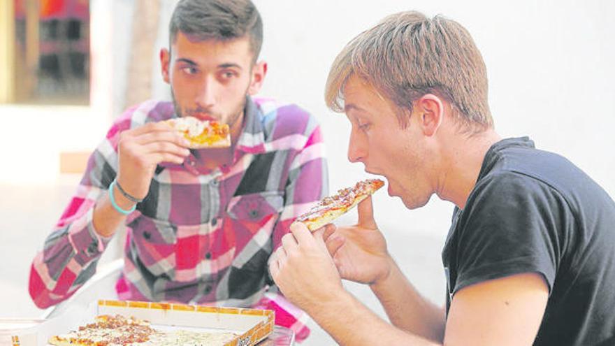 Dos jóvenes comiéndose una pizza, alimento a tomar de manera ocasional.