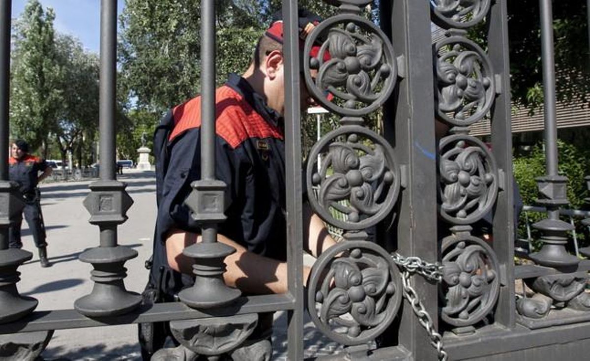 Un mosso d’esquadra col·loca cadenes a les portes del parc de la Ciutadella per evitar l’accés al recinte.