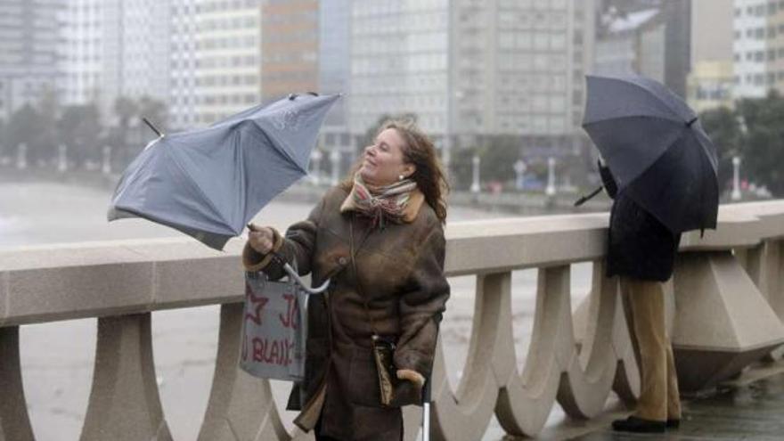 Una mujer con el paraguas estropeado por el fuerte viento en el paseo marítimo de A Coruña. / juan varela