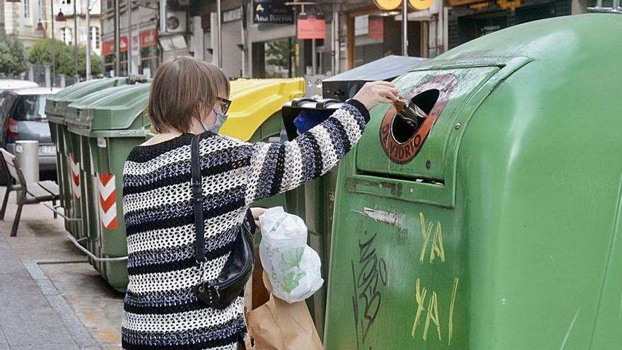 Una ciudadana deposita botellas en el colector verde, colaborando con el reciclaje de vidrio.