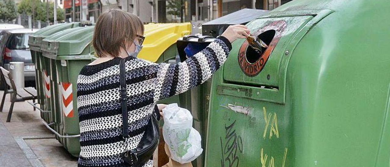 Una ciudadana deposita botellas en el colector verde, colaborando con el reciclaje de vidrio.