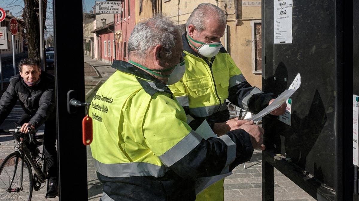 Funcionarios de Lombardía protegidos con máscaras colocan carteles en San Fiorano, una de las localidades en cuarentena en Italia, el 24 de febrero del 2020