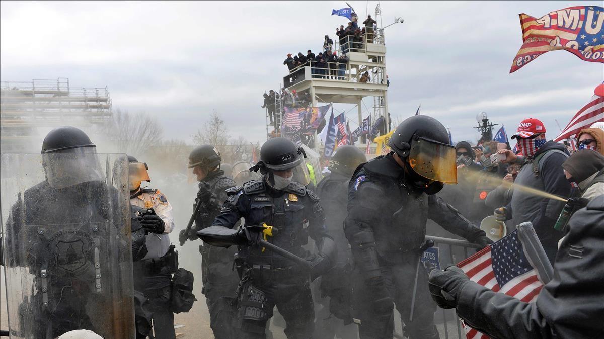 Los manifestantes rocían espráis y tiran diversos objetos contra los agentes de policía que intentan disolver a los manifestantes apostados frente al Capitolio.