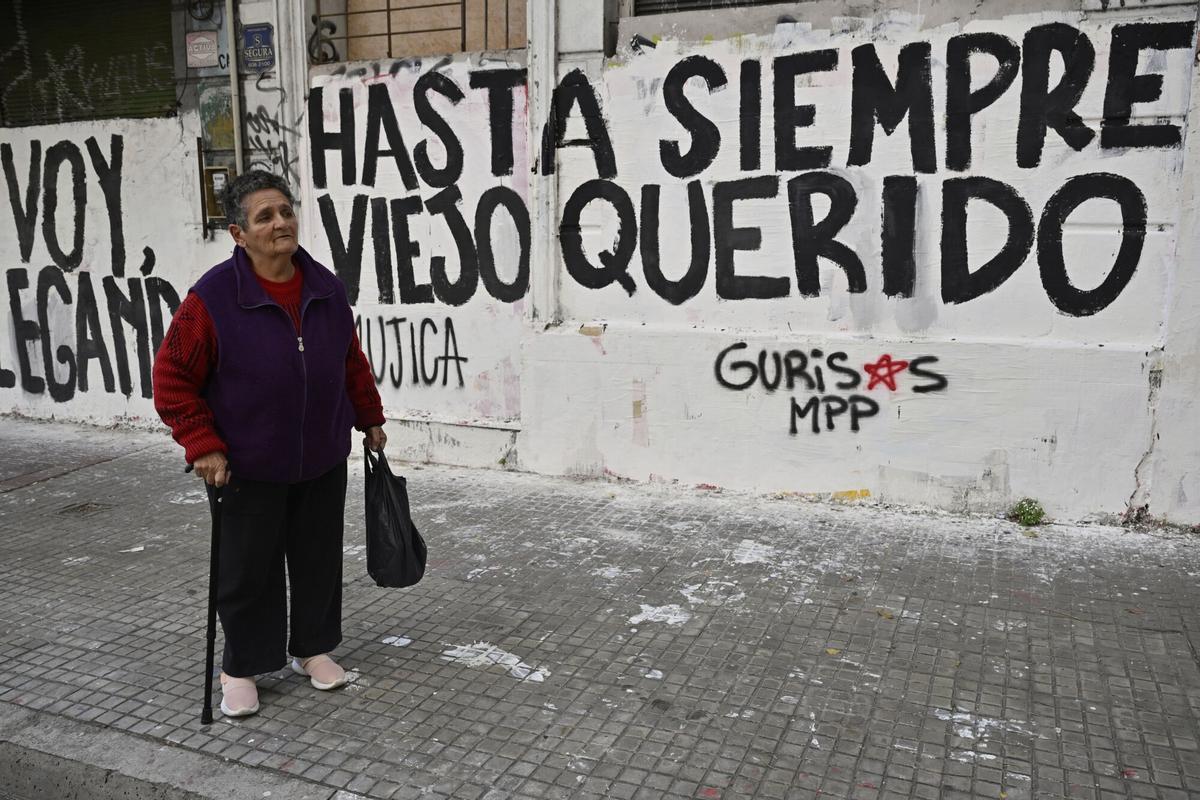 A woman watches the funeral procession of former President Jose Mujica from the presidential palace to the National Assembly, next to graffiti that reads in Spanish: Farewell dear old man, in Montevideo, Uruguay, Wednesday, May 14, 2025. (AP Photo/Santiago Mazzarovich)