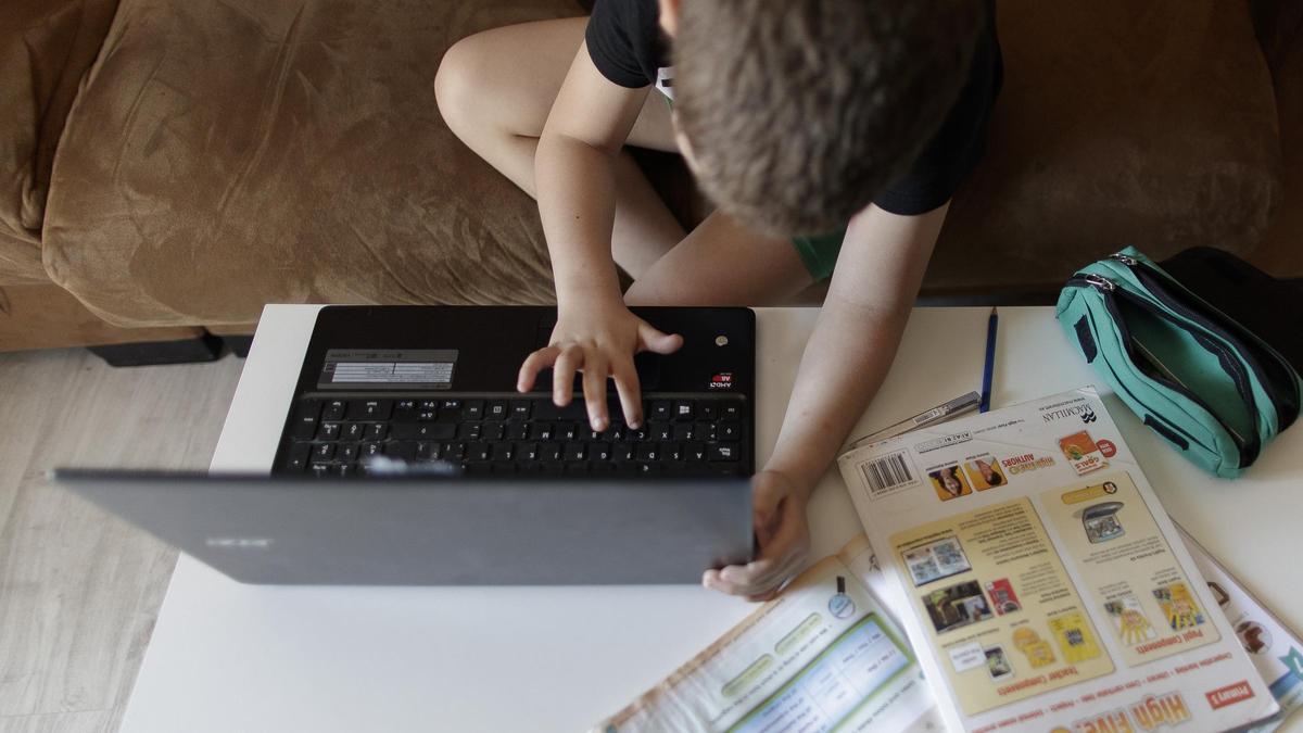 Un niño consulta su portátil mientras realiza tareas de inglés en su casa.