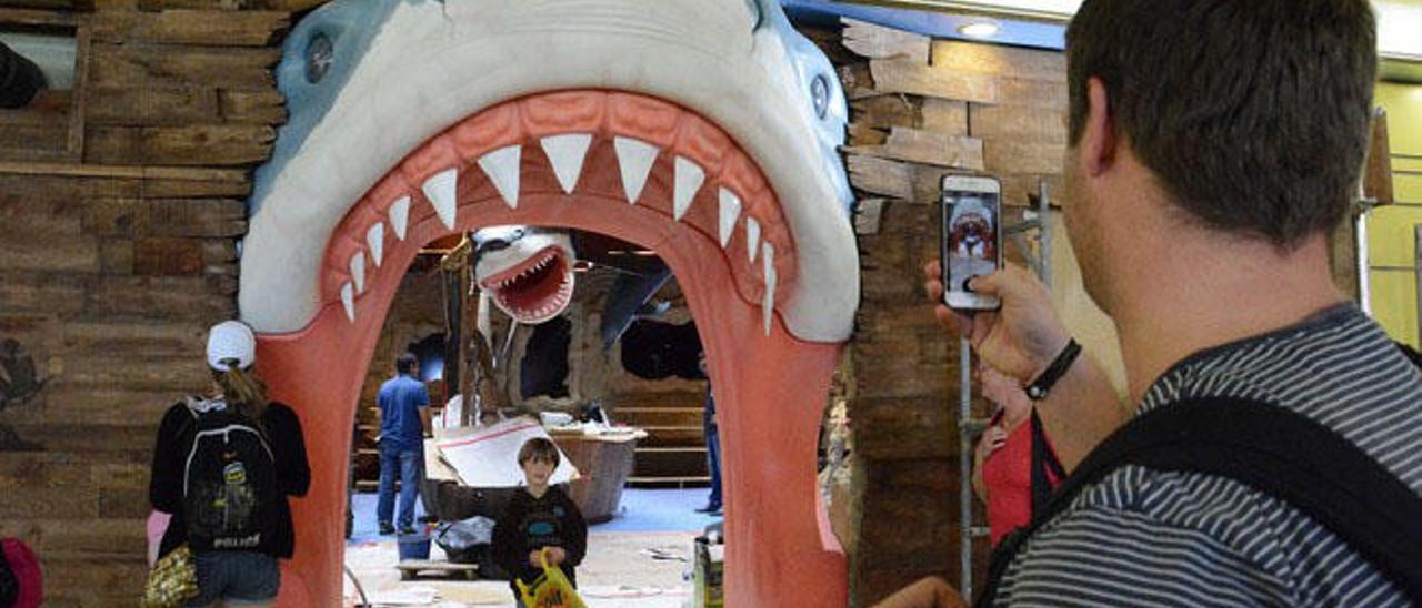 Un turista saca una foto a un niño en la entrada del negocio bajo la mandíbula del tiburón.