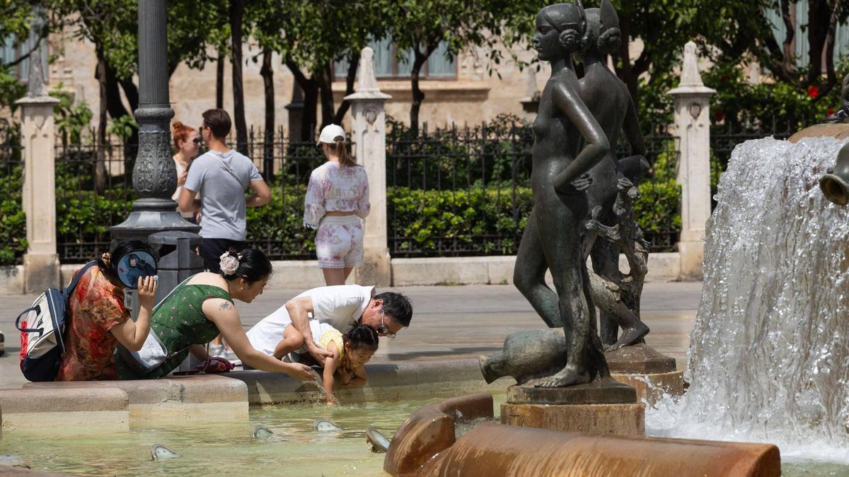 Una familia de turísticas asiáticos ayer jugando con el agua de la fuente del Túria de Silvestre de Edeta en la plaza de la Mare de Déu de València.