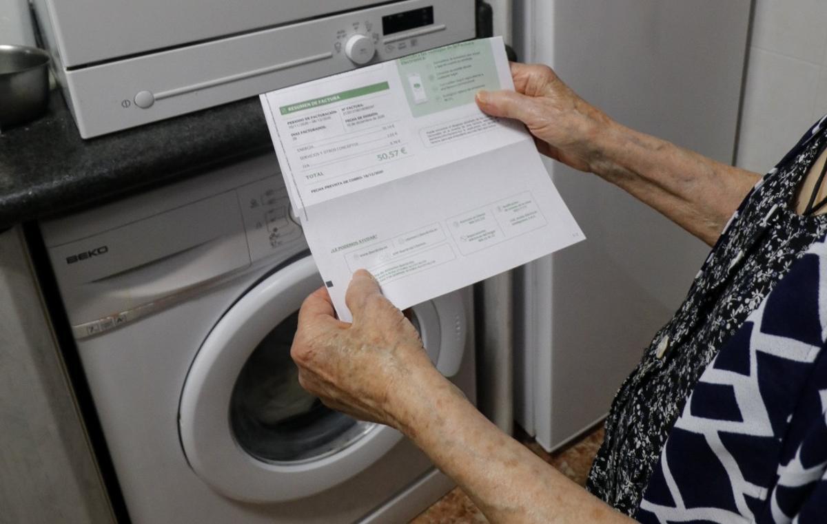 Una persona mayor mira la factura de la electricidad mientras calcula cuándo poner la lavadora para minimizar el gasto en esta energía.