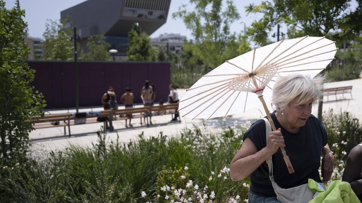 Una mujer se refugia del sol bajo un paraguas mientras pasea por el parque de Glories de Barcelona.