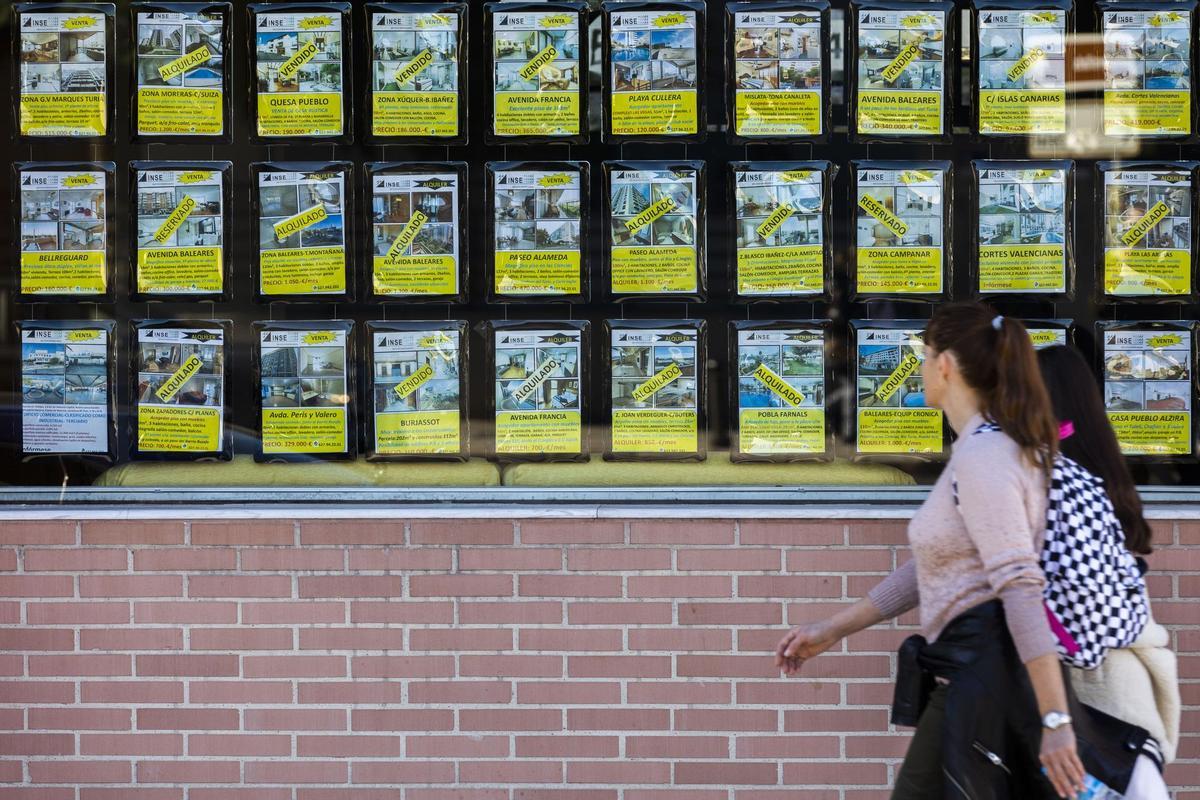 Dos mujeres pasean frente a carteles de una inmobiliaria.