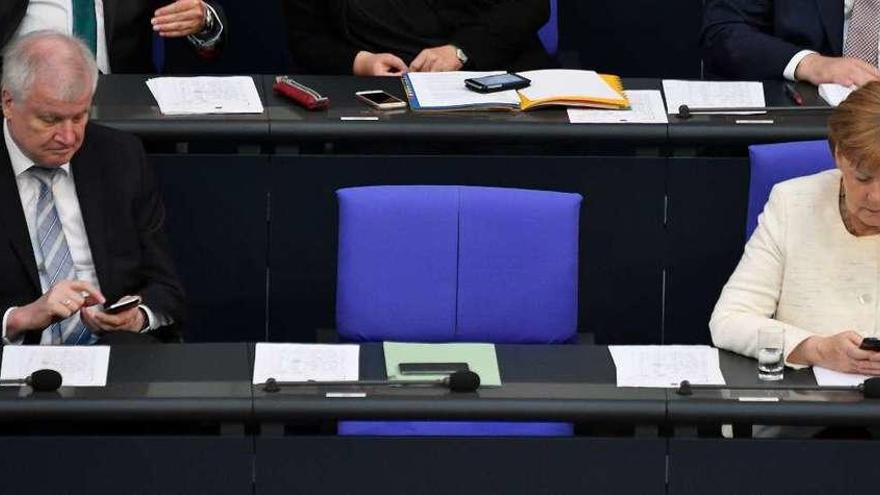 Seehofer y Merkel teclean en sus móviles durante una sesión en el Bundestag. // AFP