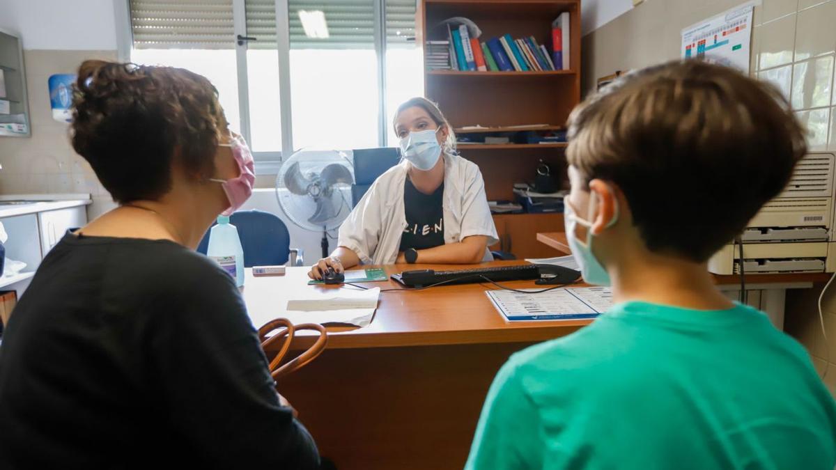 Una médico atiende en la consulta a un menor acompañado por su madre.