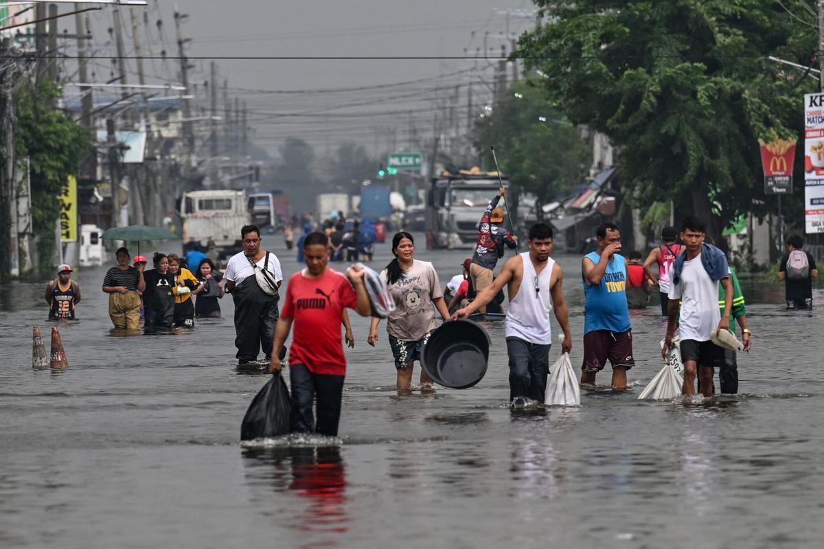 La gente camina a través de una calle inundada después de las fuertes lluvias traídas por el monzón del suroeste en Pampanga el 31 de agosto de 2026. (Foto de Jam STA ROSA / AFP)