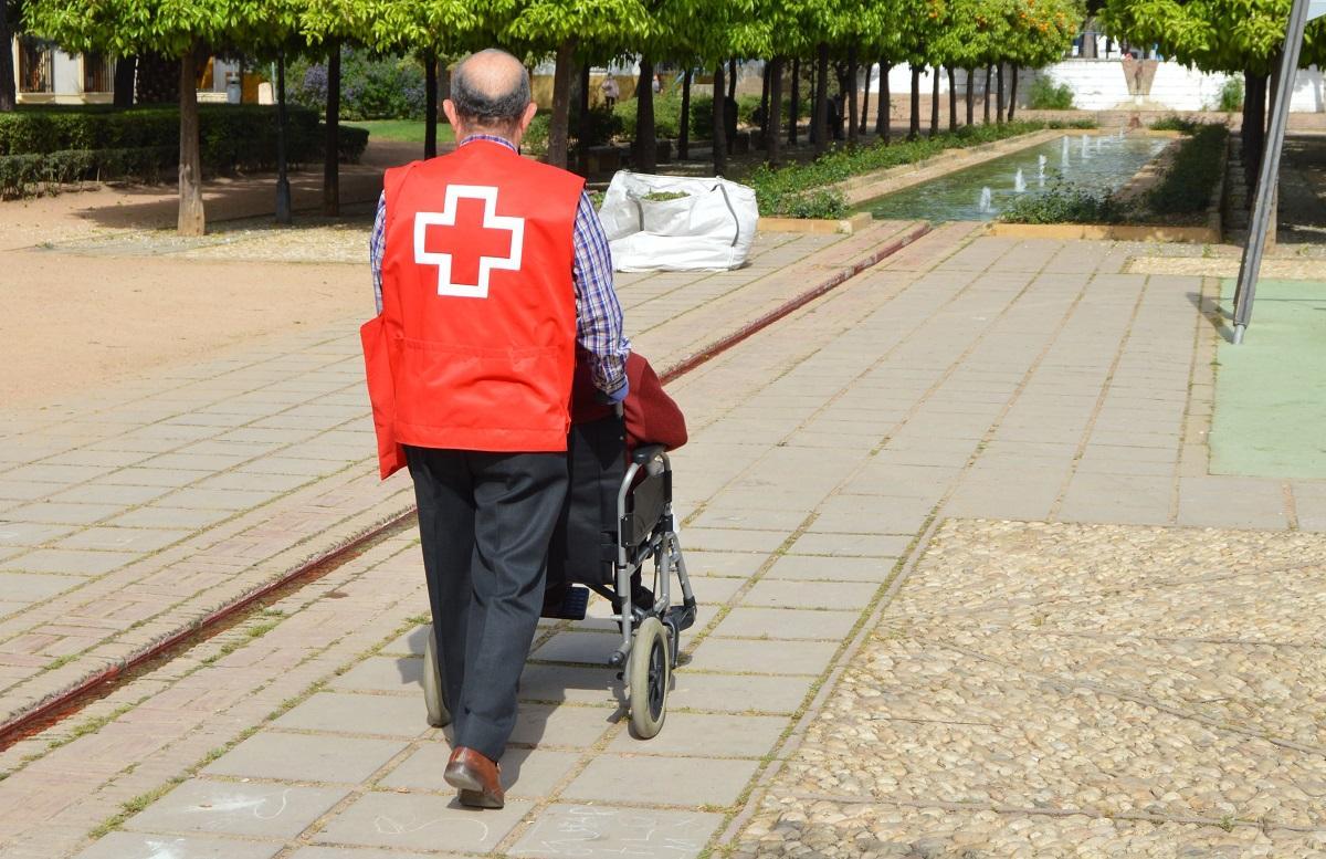 Un voluntario de Cruz Roja pasea a una persona mayor en una silla de ruedas.