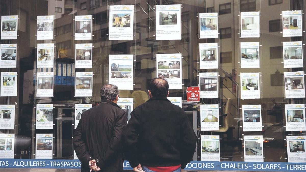 Dos hombres consultan los anuncios en el escaparate de una inmobiliaria de Vigo