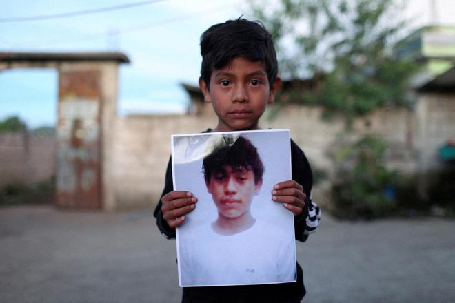 Un niño de Guatemala sostiene un cartel con la imagen de un familiar, encontrado en un camión junto con otros cadáveres de migrantes en Texas.