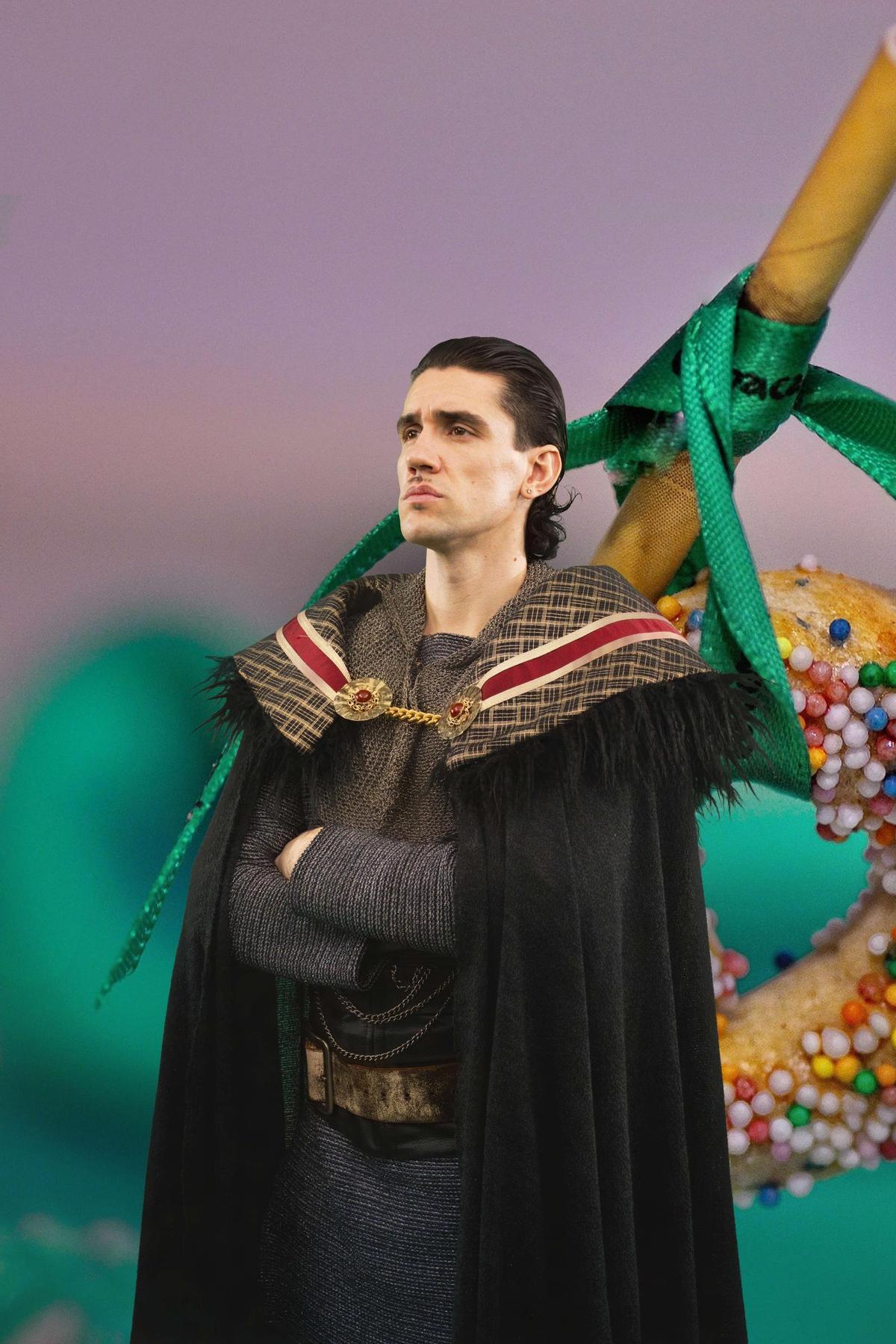 El cantante, con un disfraz medieval junto a una caña con la cinta verde.