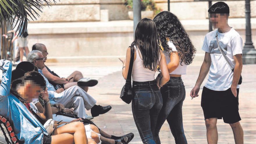 Un grupo de jóvenes, algunos sin mascarilla, bromea ayer, junto a unos mayores, en un banco de la plaza del Ayuntamiento de València.