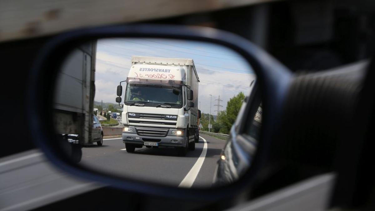 Un camión, visto en el espejo retrovisor de un turismo mientras circula por una autovía.