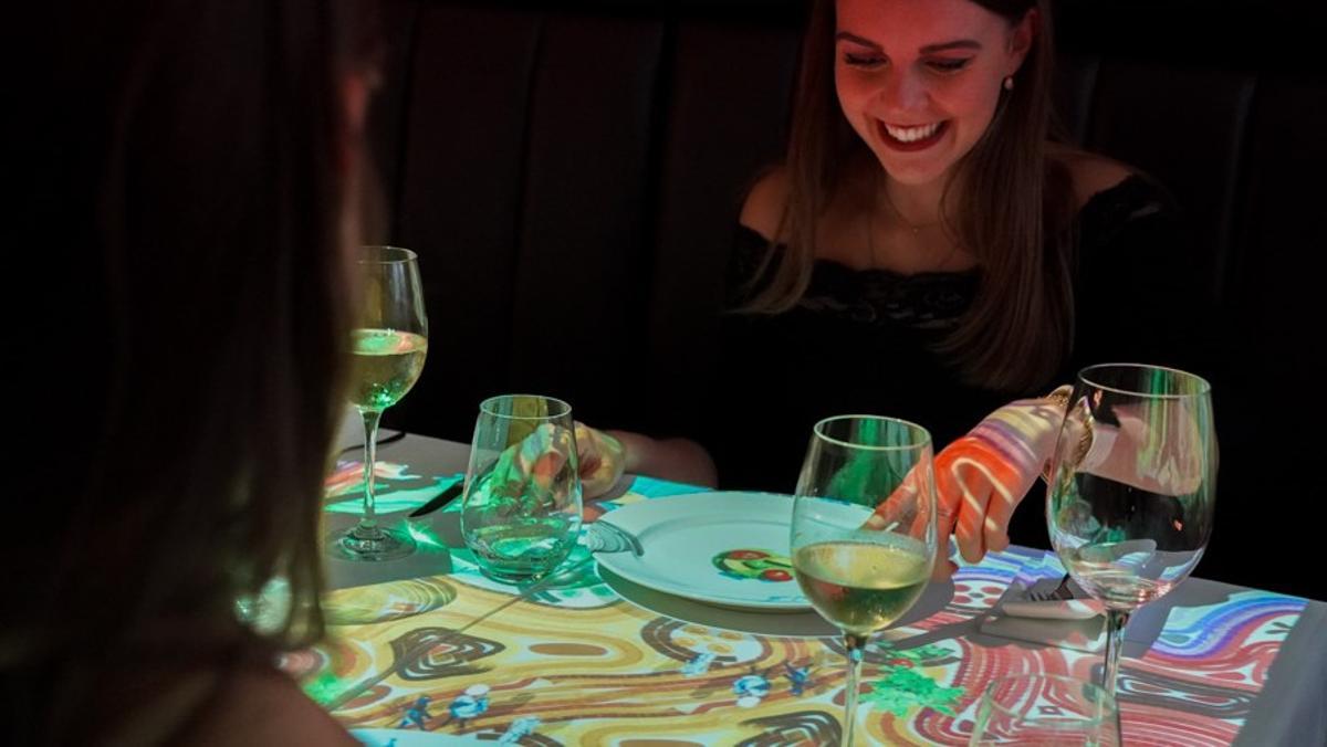 Dos comensales, sorprendidas con las proyecciones sobre la mesa de 'Le Petit Chef & Friends'.