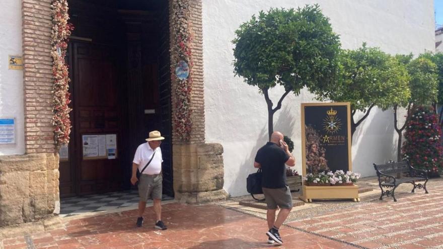Dos turistas pasan junto al  cartel que anuncia la coronación de la Virgen, en la iglesia de La Encarnación.