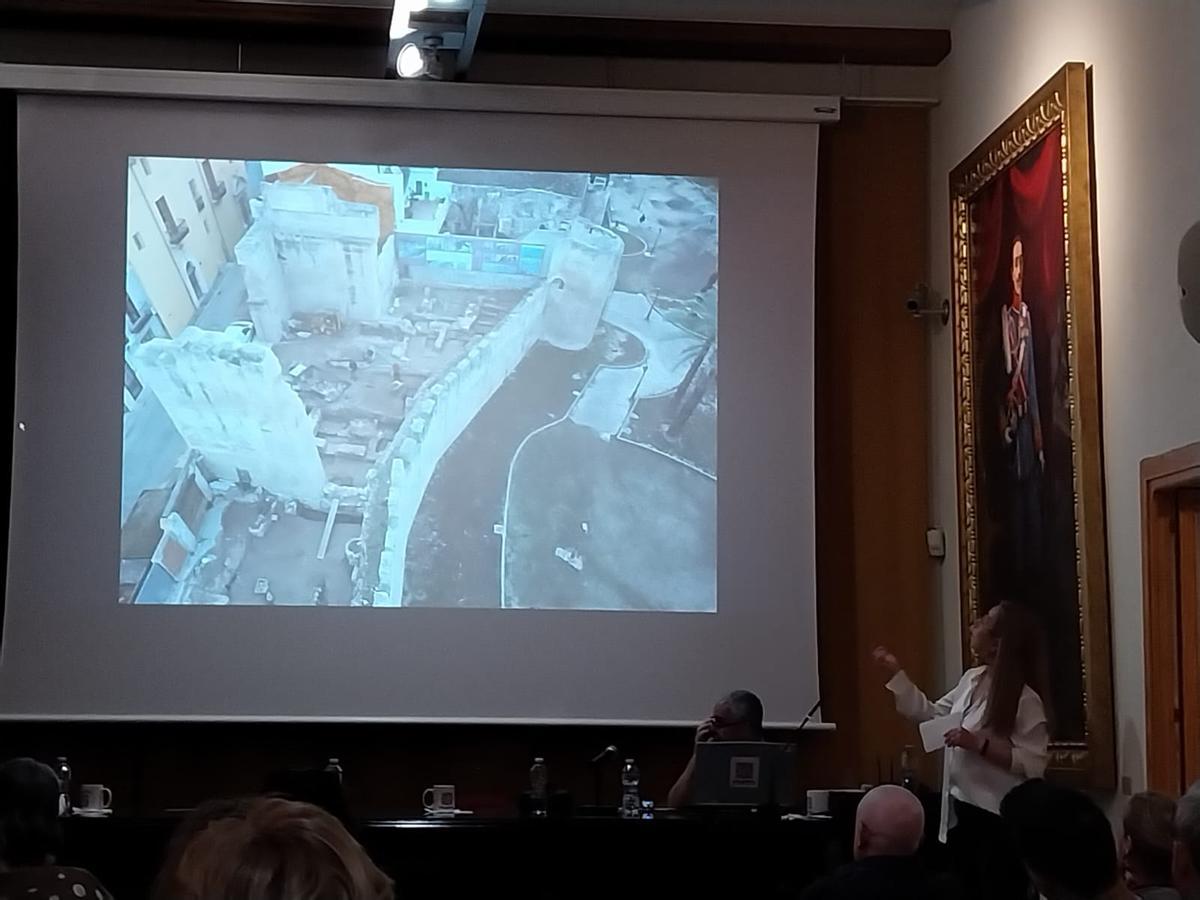 La arqueóloga María Clausi, durante su exposición. En la pantalla, una vista aérea de las excavaciones.