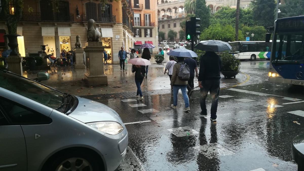 Peatones atraviesan el Passeig del Born protegidos de la lluvia con paraguas.