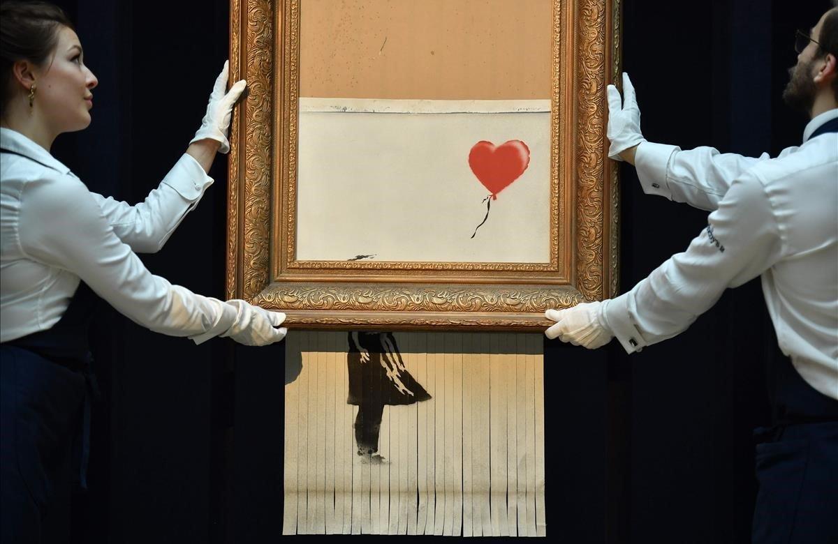 Empleados de Sotheby’s posan con la obra recién terminada del artista Banksy titulada ’Love is in the Bin’, una obra que se creó cuando la pintura ’Girl with Balloon’ fue pasada a través de una trituradora.