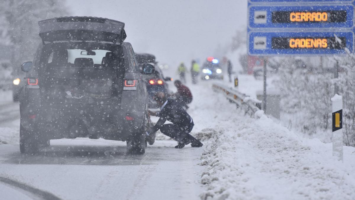 Varias personas ponen cadenas a los coches en una carretera nevada