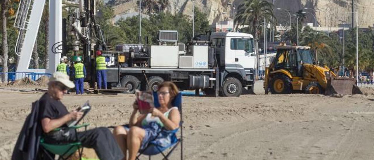 Dos personas disfrutan de la jornada primaveral en la playa del Postiguet, junto a las obras relativas a los lavapiés. álex domínguez