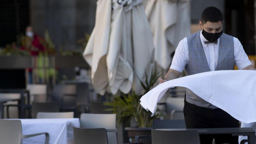 Un camarero prepara una  mesa en una terraza.