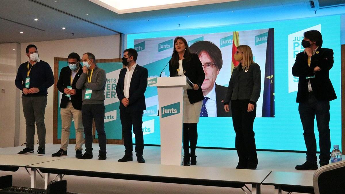 Pla general de l&#039;escenari on JxCat va valorar la nit electoral del 14-F, amb la candidata, Laura Borràs; en pantalla, Puigdemont