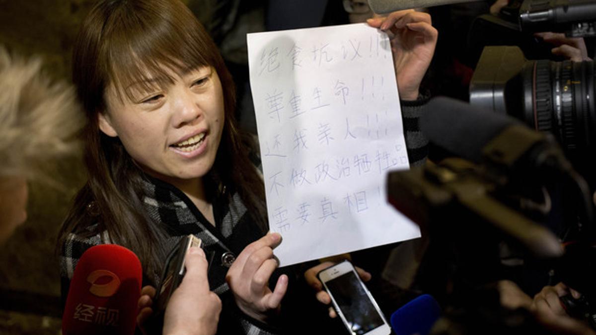 Una familiar de un pasajero del vuelo MH370 muestra a los periodistas un papel en el que se anuncia una huelga de hambre y se pide a las autoridades que digan la verdad, este martes en Pekín.