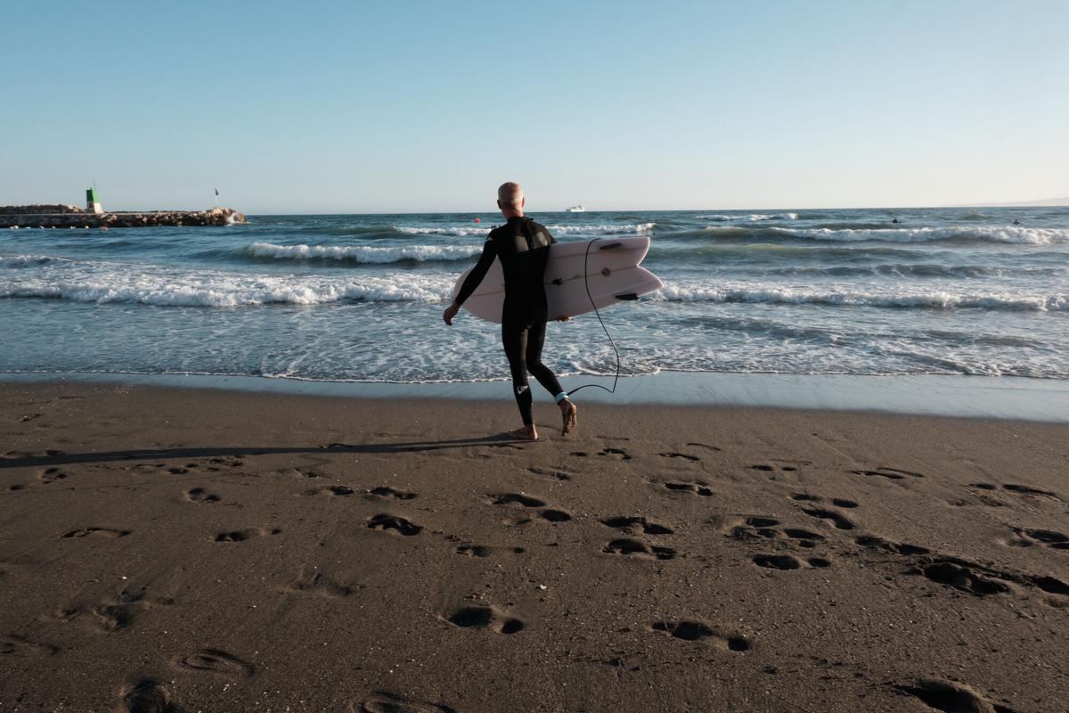Un surfista se dispone a entrar al agua con un traje de neopreno