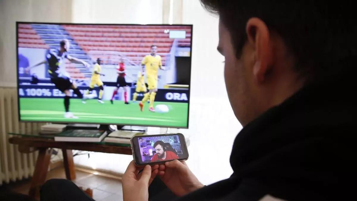 Un joven sigue un partido de fútbol por televisión y mira una intervención del 'influencer' Ibai Llanos en el móvil.