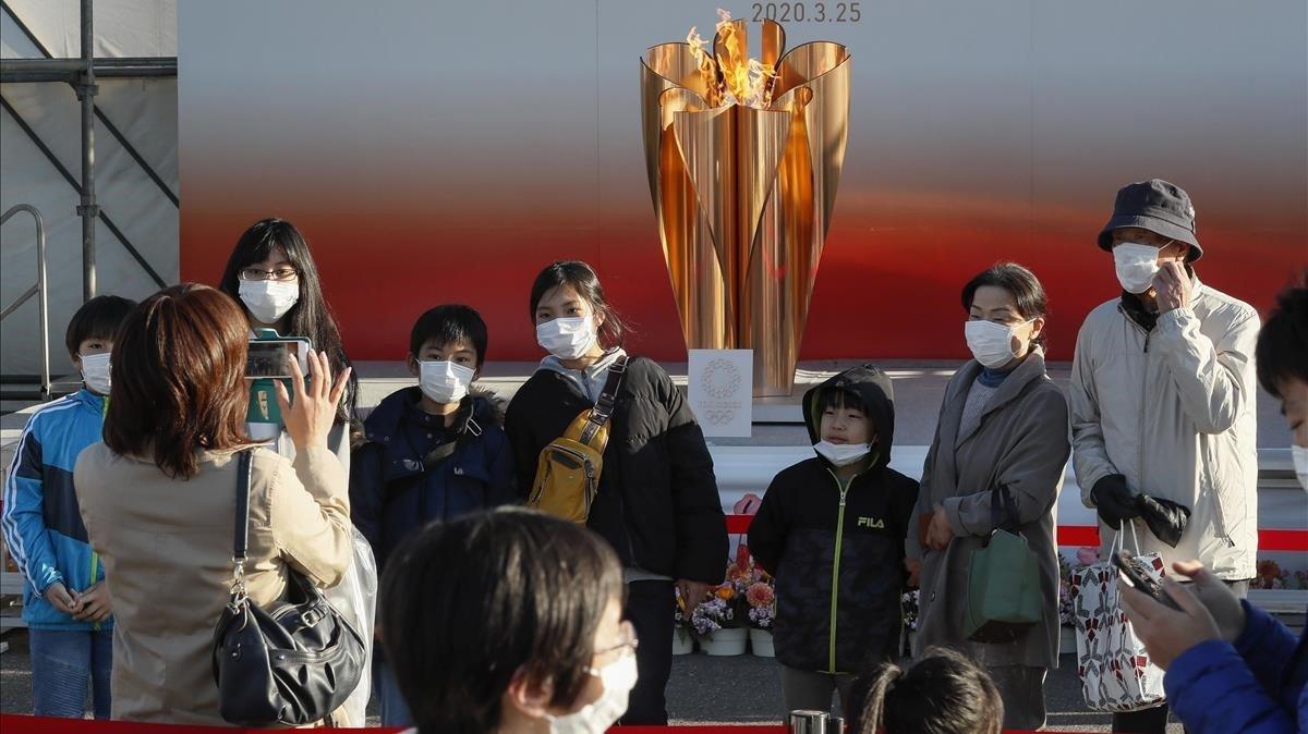 Ciudadanos japoneses se fotografian ante la antorcha olímpica debidamente protegidos.