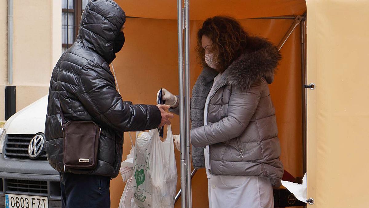 Una empleada de Cáritas entrega la ración diaria de alimentos a un joven.