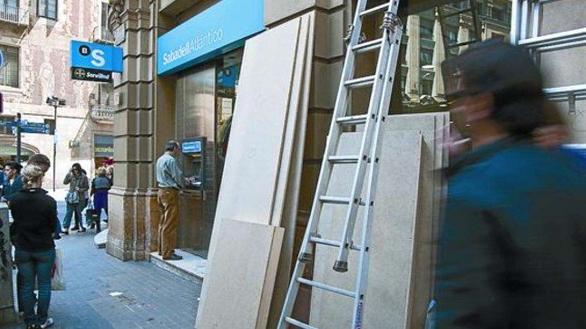 Preparativos para proteger de hipotéticos destrozos una oficina bancaria en la Via Laietana, ayer.