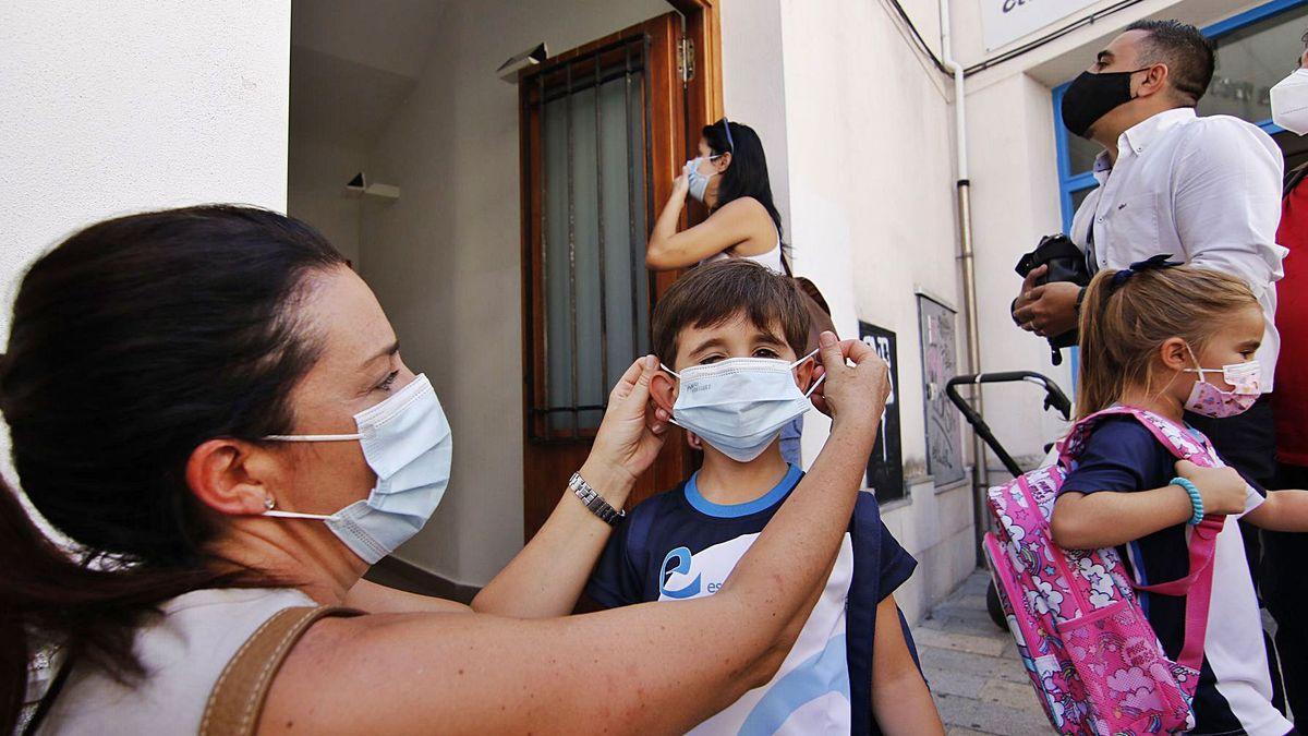 Una madre coloca una mascarilla a la entrada de un colegio.