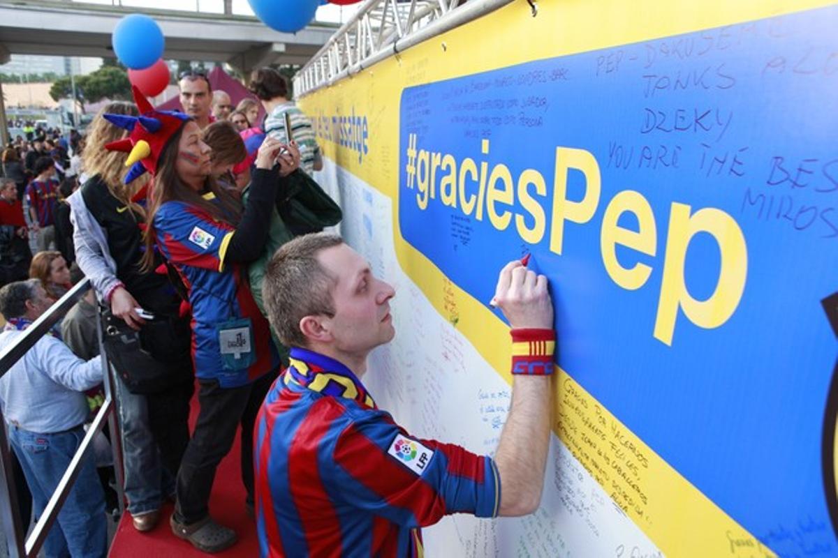 Un aficionat del Barcelona escriu un missatge de comiat a Pep Guardiola al mur que s’ha posat al Camp Nou per homenatjar el tècnic.