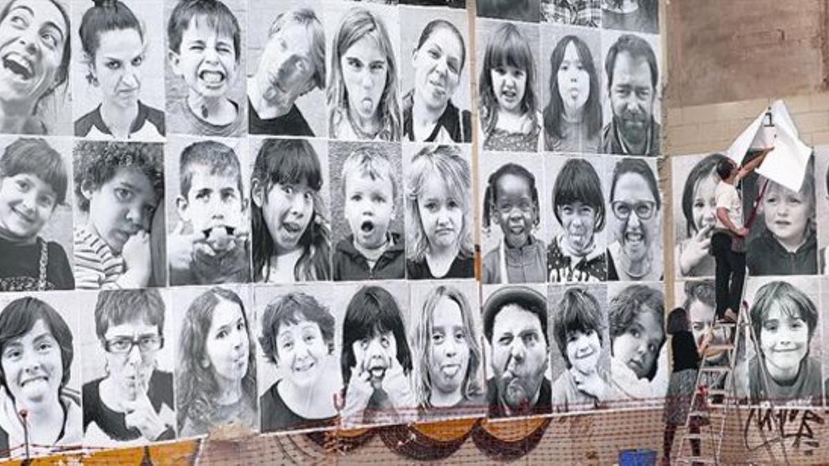 Un hombre y una mujer pegan grandes retratos de alumnos, profesores y padres de la escuela Àngel Baixeras en un solar de Ciutat Vella.