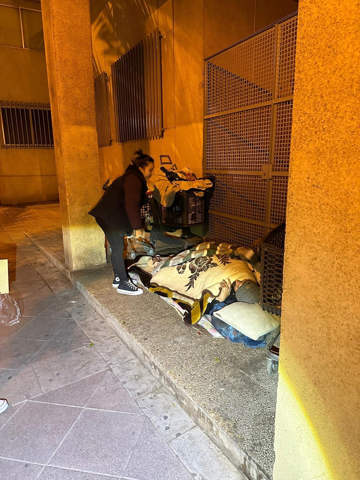 Una voluntaria se entrevista con un indigente que duerme junto a la fachada del instituto Carrús, en Elche