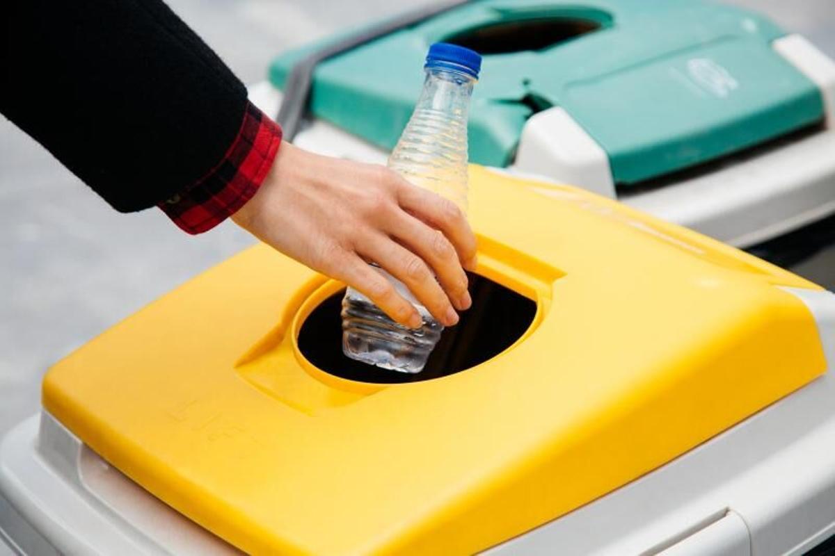 Una persona deposita una botella de agua vacía en el contenedor de plásticos. | l. o. RECOGIDA DE BASURA. CONTENEDORES. RECICLAJE