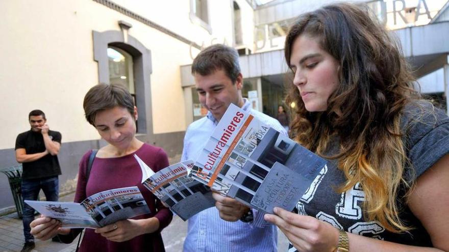 Tres jóvenes ojean la publicación con la programación cultural de Mieres.