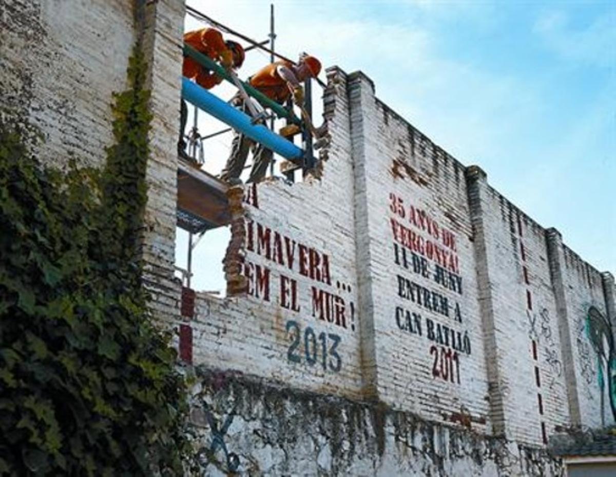 Dos operaris inicien l’enderrocament del mur de Can Batlló, que obrirà el recinte al barri, ahir al matí.