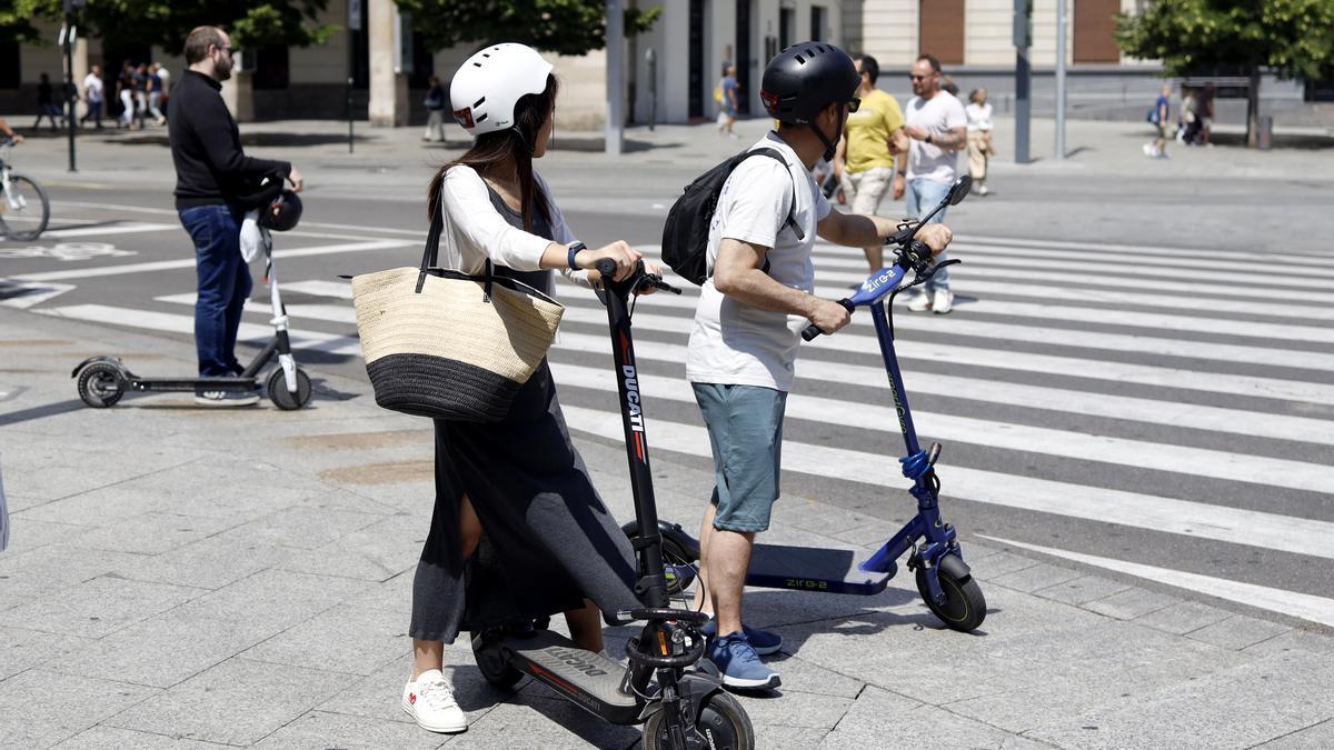 Dos personas esperan con su patinete a cruzar el paso de peatones.