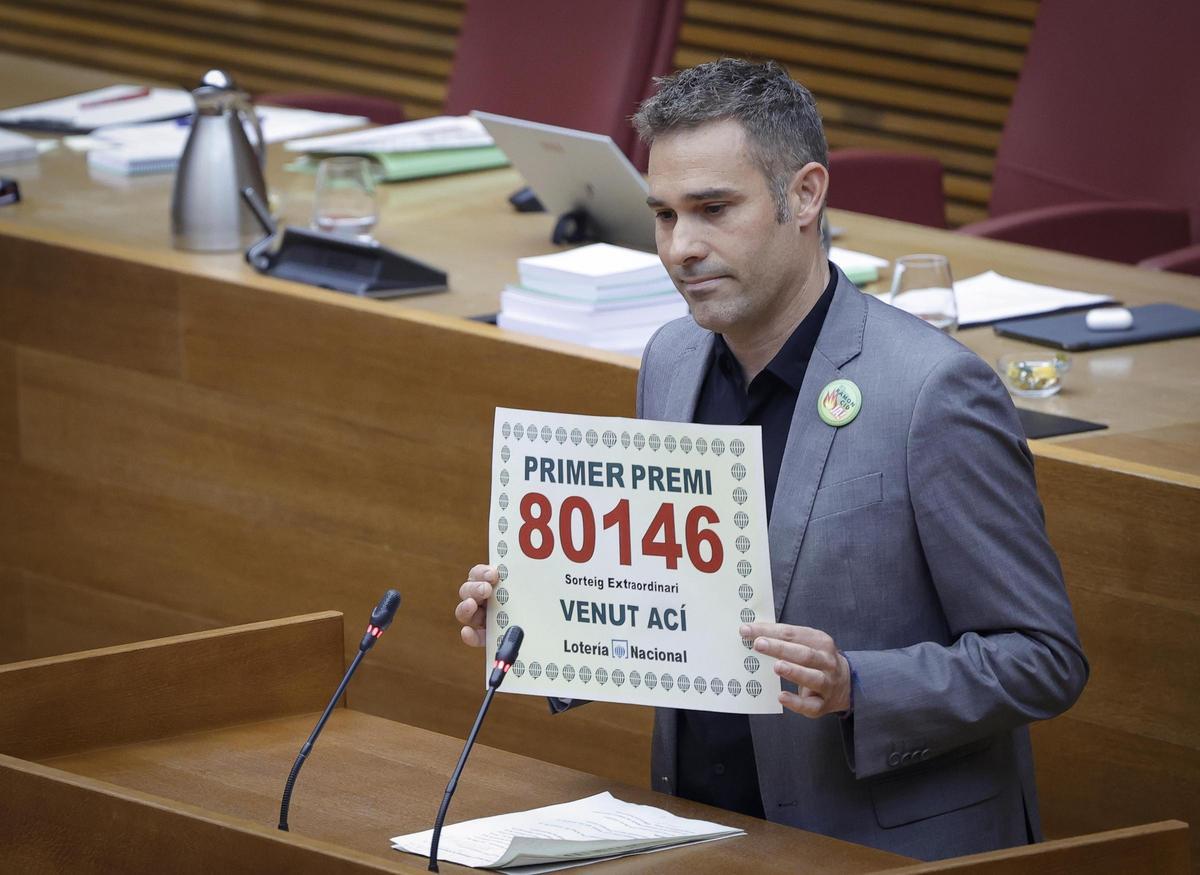 El diputado de Compromís, Gerard Fullana, muestra un 'décimo' con el sueldo de la consellera en las Corts.